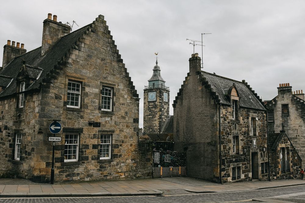 Historic stone buildings along a cobblestone street in Edinburgh's Old Town under overcast skies.