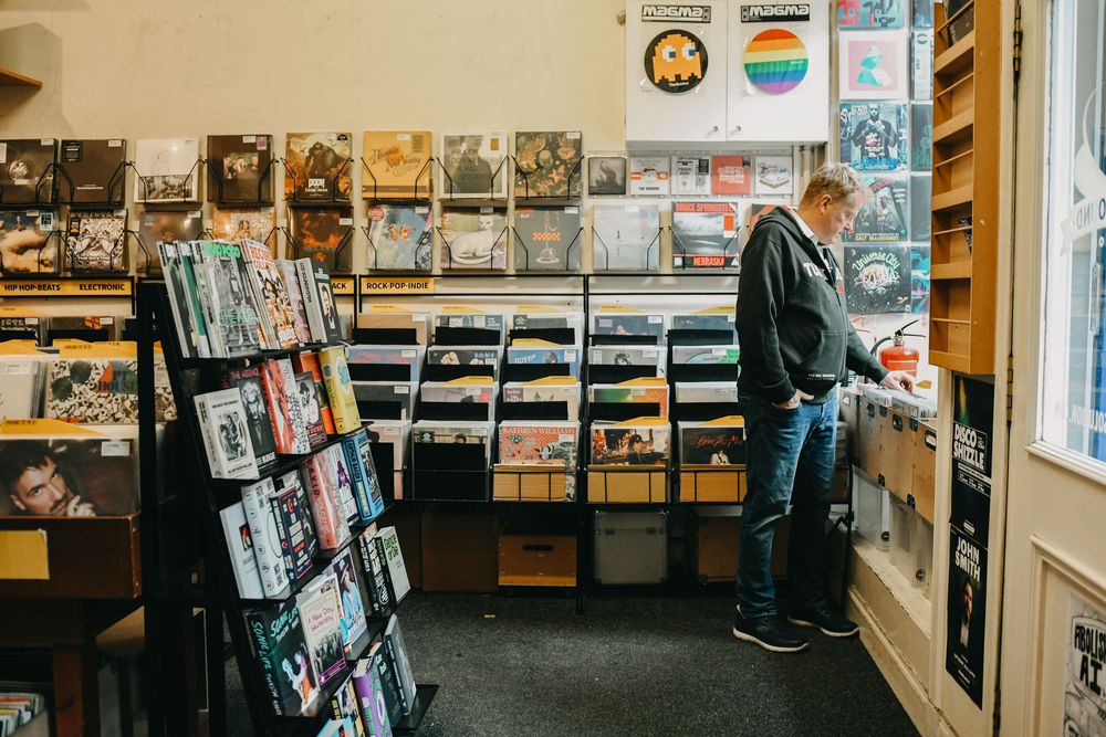 Person browsing vinyl records in a cozy independent music store with shelves full of albums and posters on the walls.