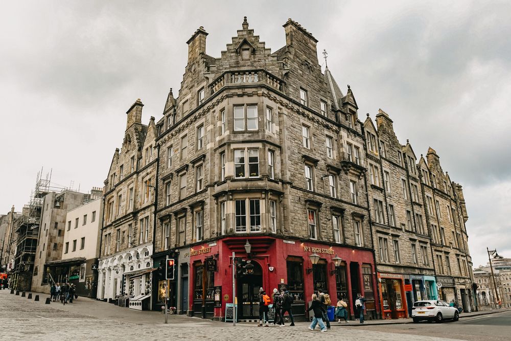 Historic stone corner building in Edinburgh's Old Town featuring ornate architecture, a red pub entrance, and cobblestone streets.