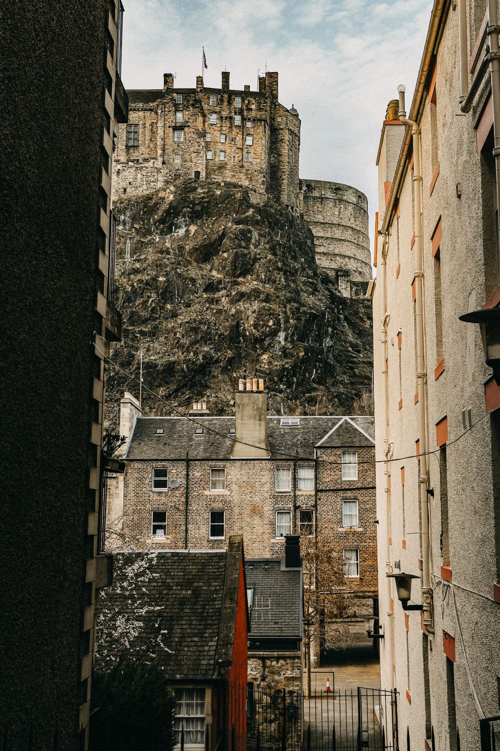 Dramatic view of Edinburgh Castle perched on volcanic rock, framed by narrow historic stone buildings in the Old Town below.