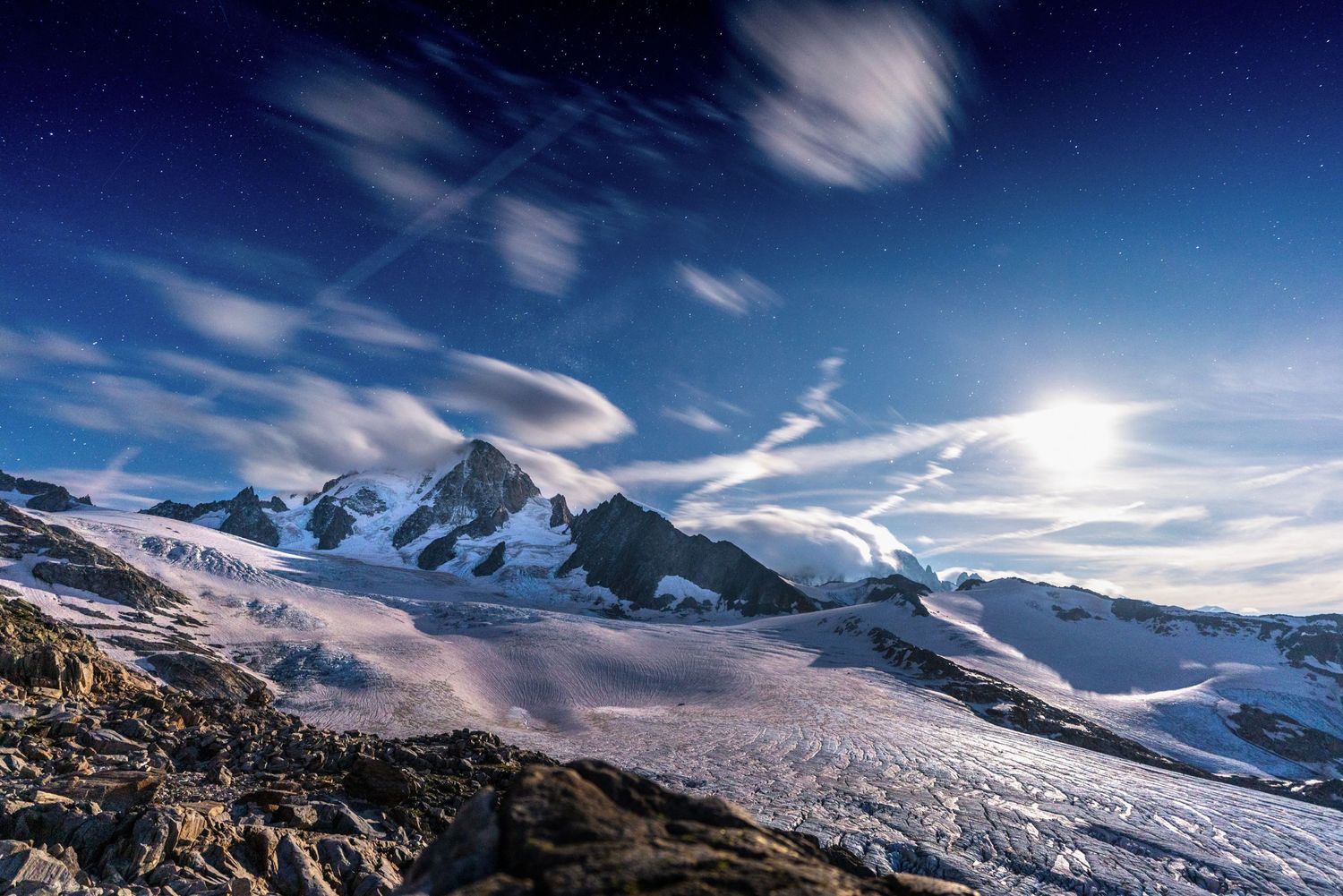 Majestic snow-covered mountain peaks under wispy clouds and bright sunlight.