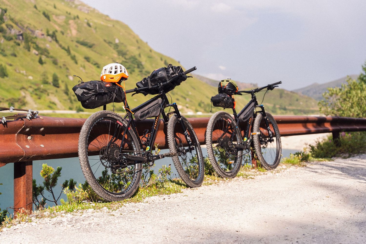 Two mountain bikes with bikepacking gear parked against a guardrail on a scenic mountain road with green hills.