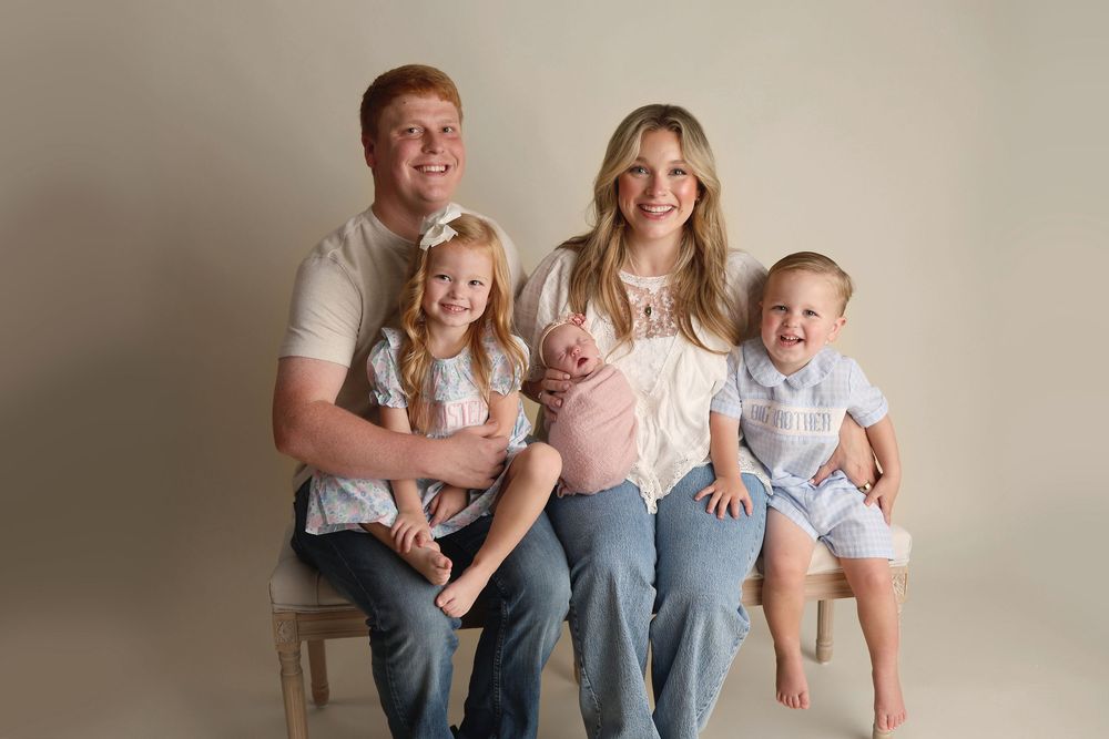 Happy family of five posing for a professional studio portrait with newborn baby, two toddlers, and parents.