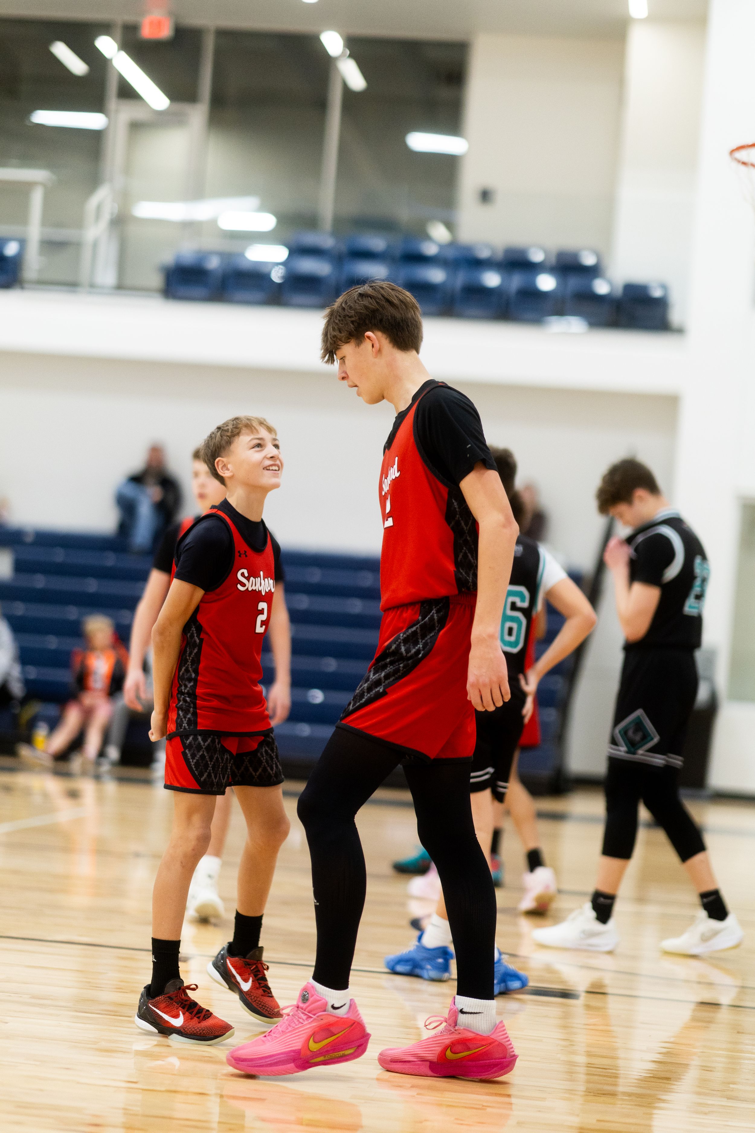 Young basketball players in red jerseys and black shorts practice drills on a shiny indoor court during training.