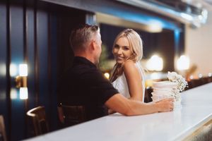 A couple shares an intimate moment together at a bar counter during what appears to be their wedding day.