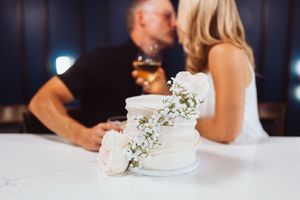 A white wedding cake decorated with delicate floral accents sits on a table at a reception.