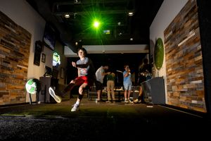 Green laser light illuminates a dark indoor skate park with brick walls and ramps where people practice skateboarding tricks.
