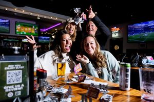 Friends enjoying drinks and food at a sports bar with multiple TV screens showing games in the background.