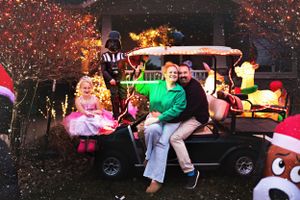 Family riding in decorated golf cart during holiday light display at night.