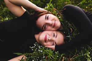 Person in black outfit laying on grass during outdoor photo session.