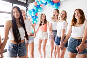 Group of friends laughing together by blue and coral balloon arch decorations.
