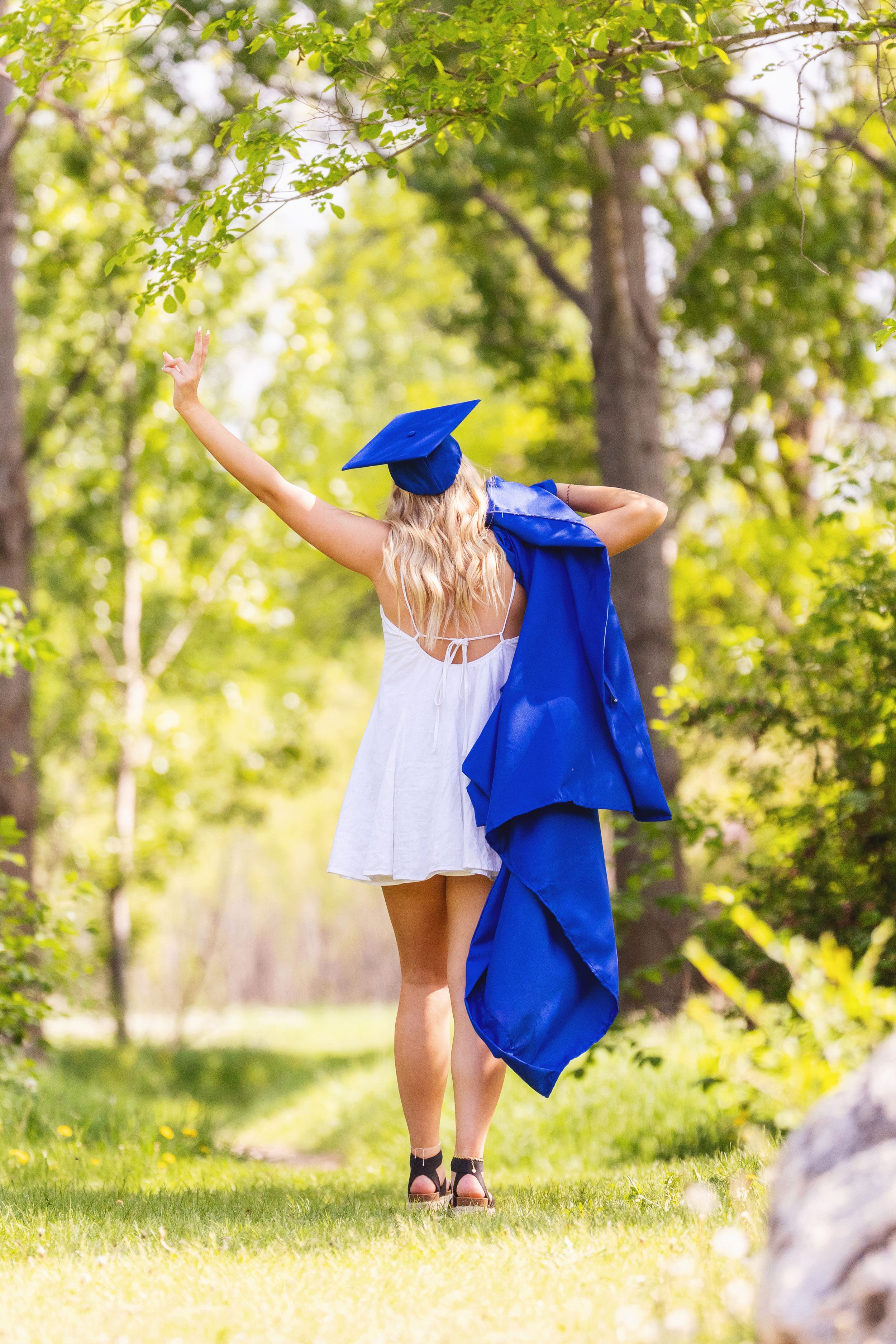 Child graduate in blue cap and gown dances joyfully across sunny park lawn in series of celebratory poses.