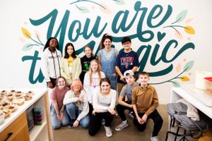 Group photo in front of teal wall with 'You are magic' text and decorative elements.