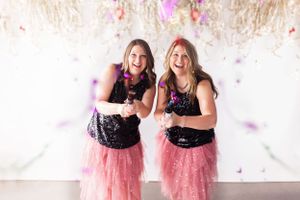 Friends in matching outfits celebrate with confetti falling around them in a studio setting.