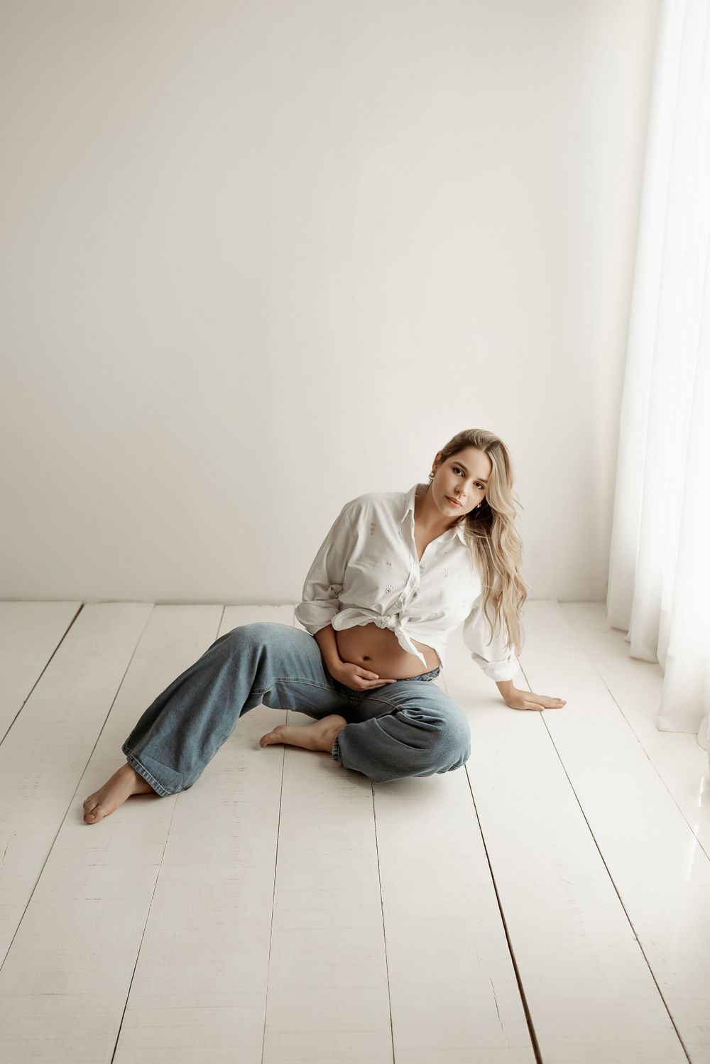 Casual maternity portrait on white wooden floor with relaxed pose.