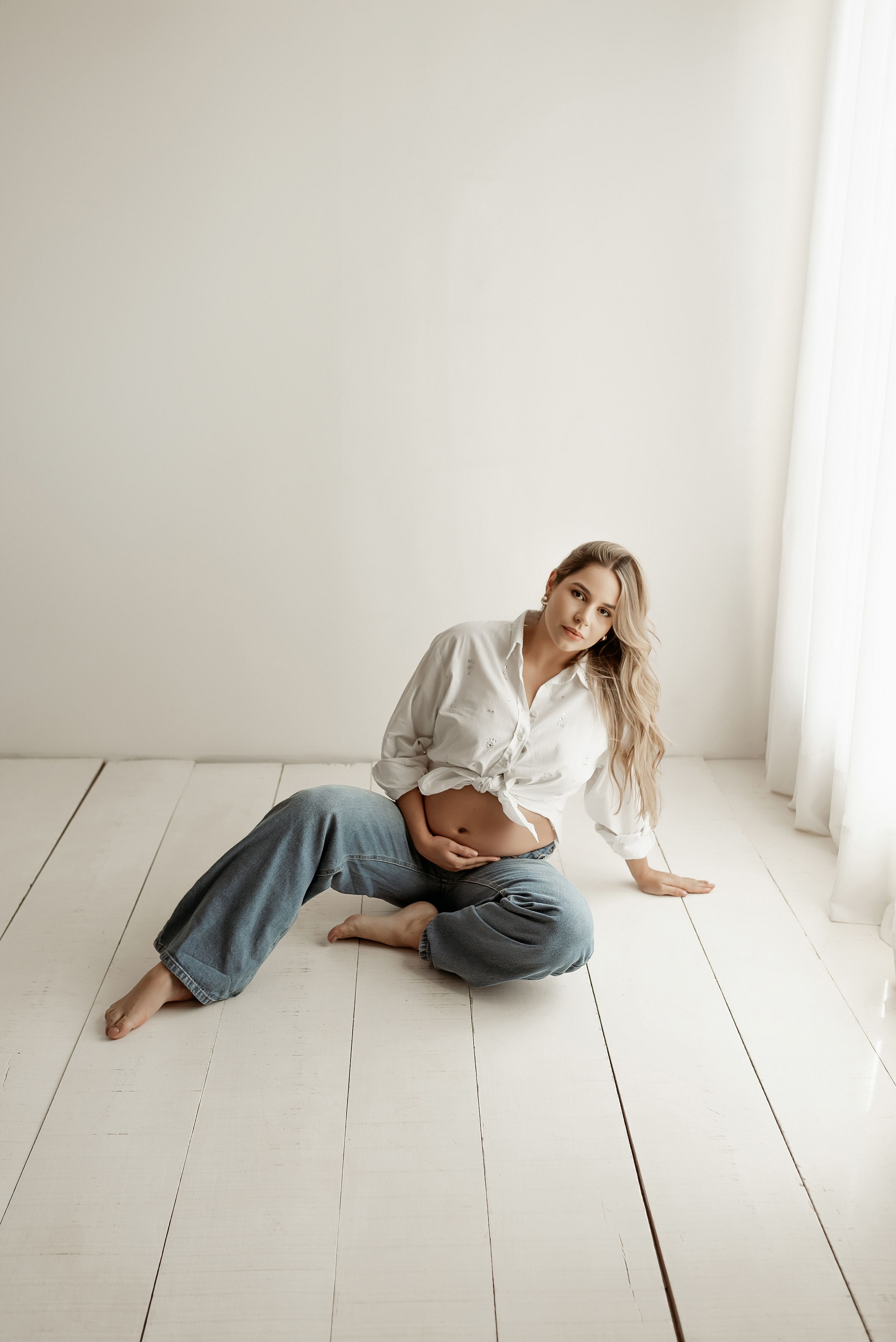 Casual maternity portrait on white wooden floor with relaxed pose.