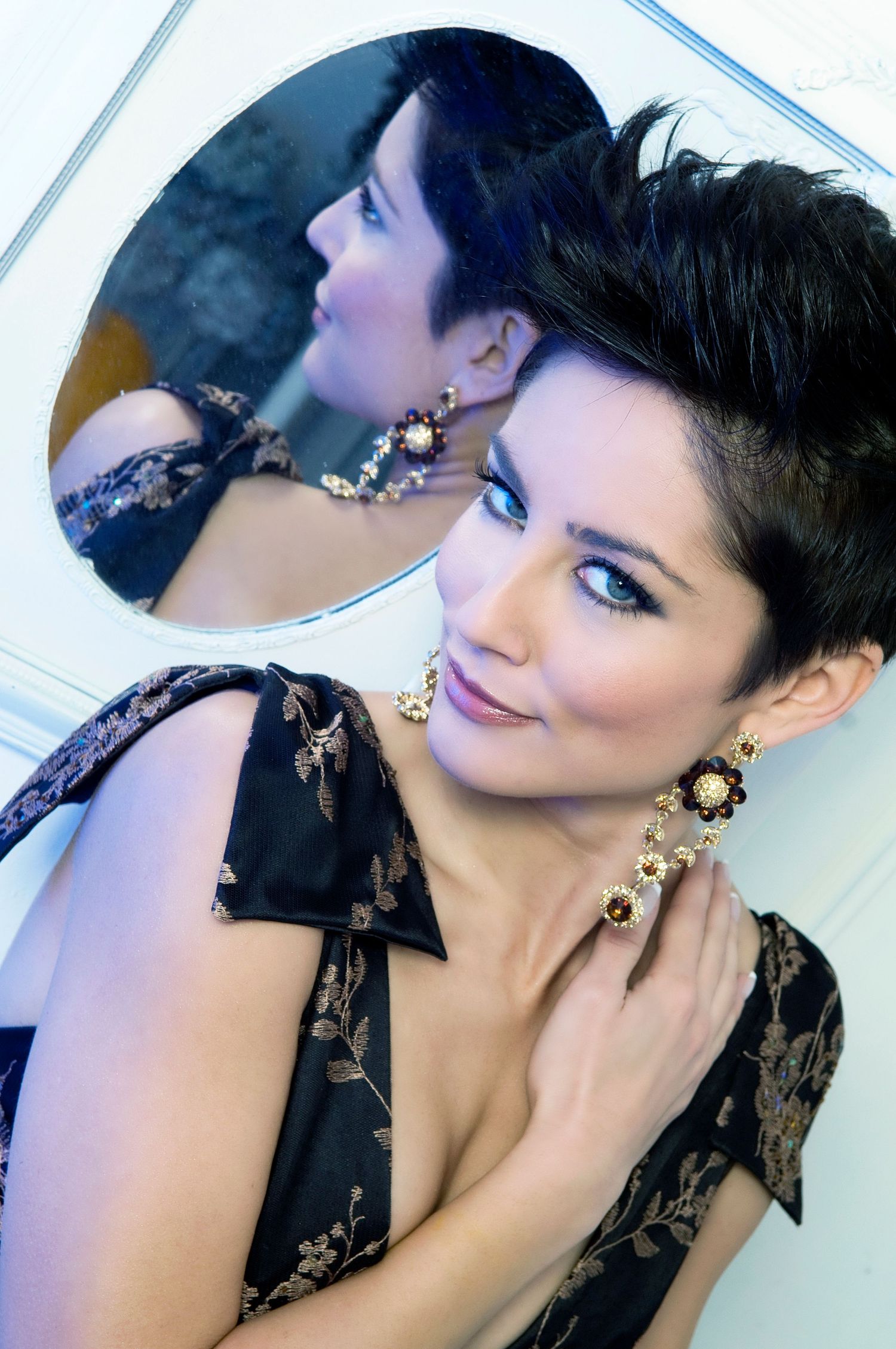 Elegant portrait with black lace dress and ornate gold jewelry reflected in mirror.