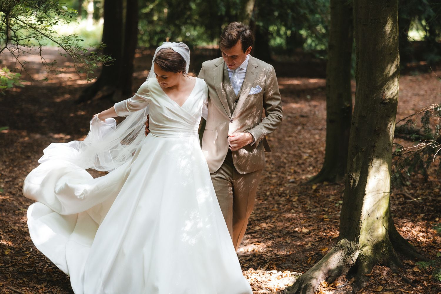 A couple shares a romantic moment in the woods with the bride's flowing white dress moving in the breeze.
