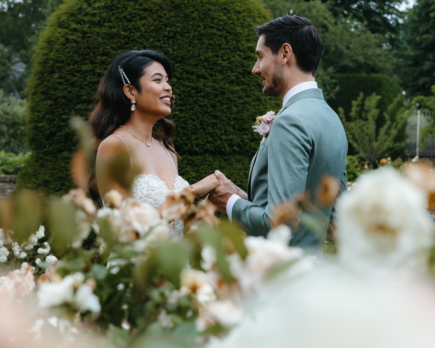 A happy couple shares an intimate moment in a garden surrounded by blooming flowers and greenery.