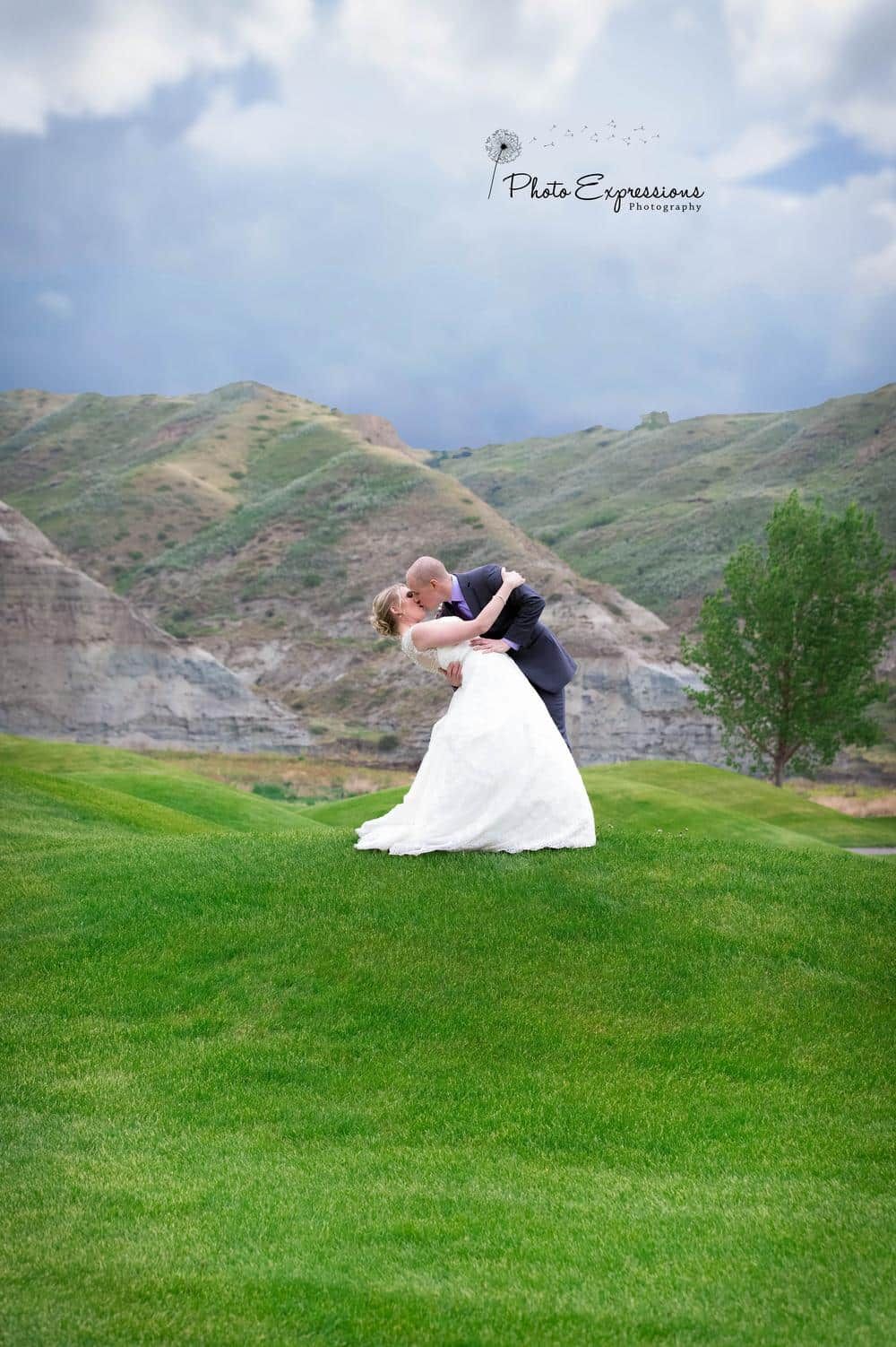 A wedding couple poses for romantic photos on a green hill with mountain views.