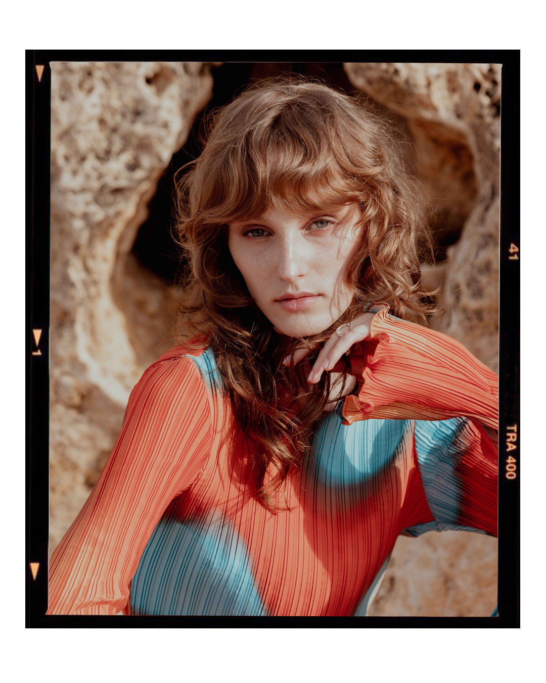 Fashion photo of a model in orange and blue patterned clothing against a rocky backdrop.