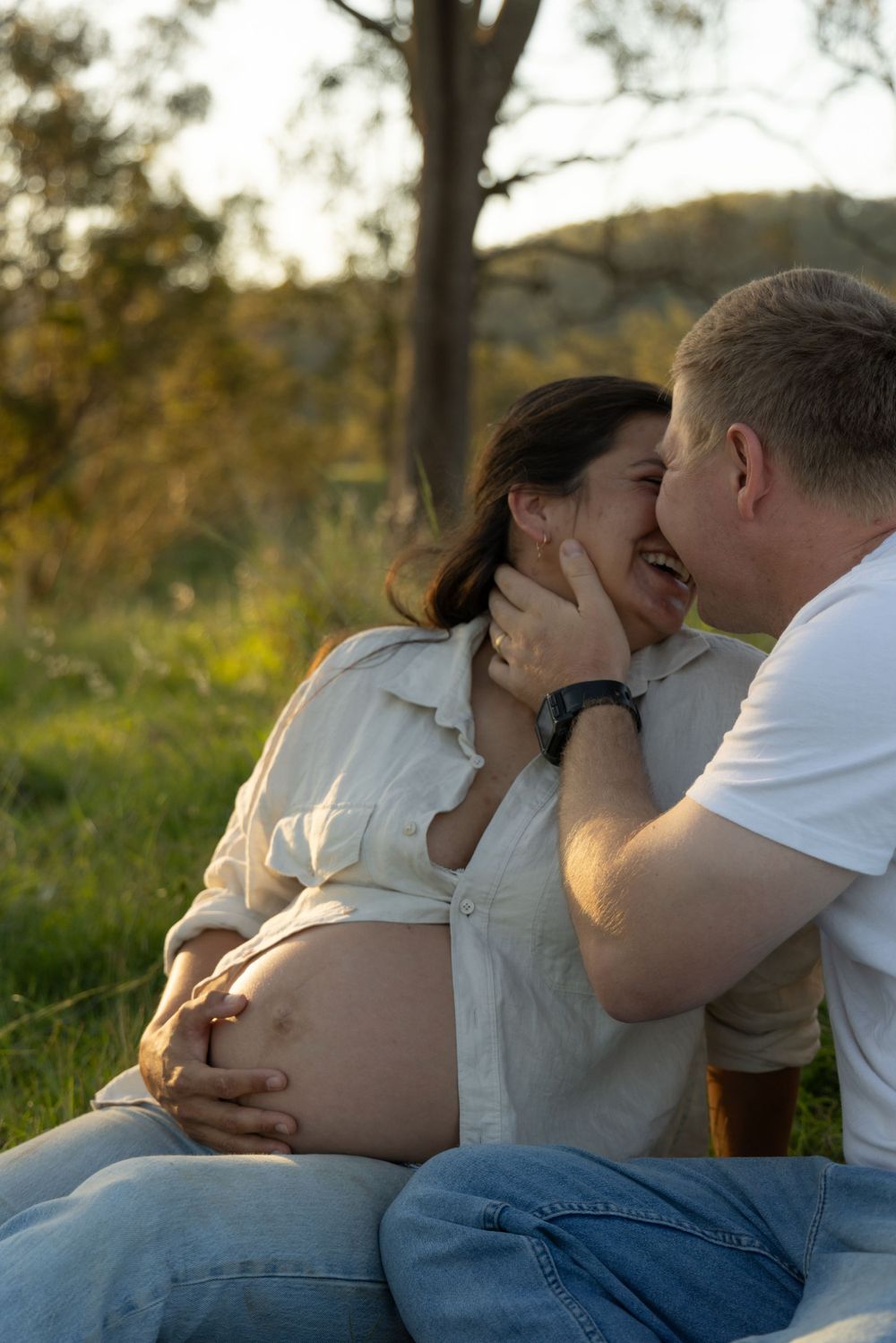 An intimate maternity photo session captures a tender moment between expectant parents at sunset in nature.