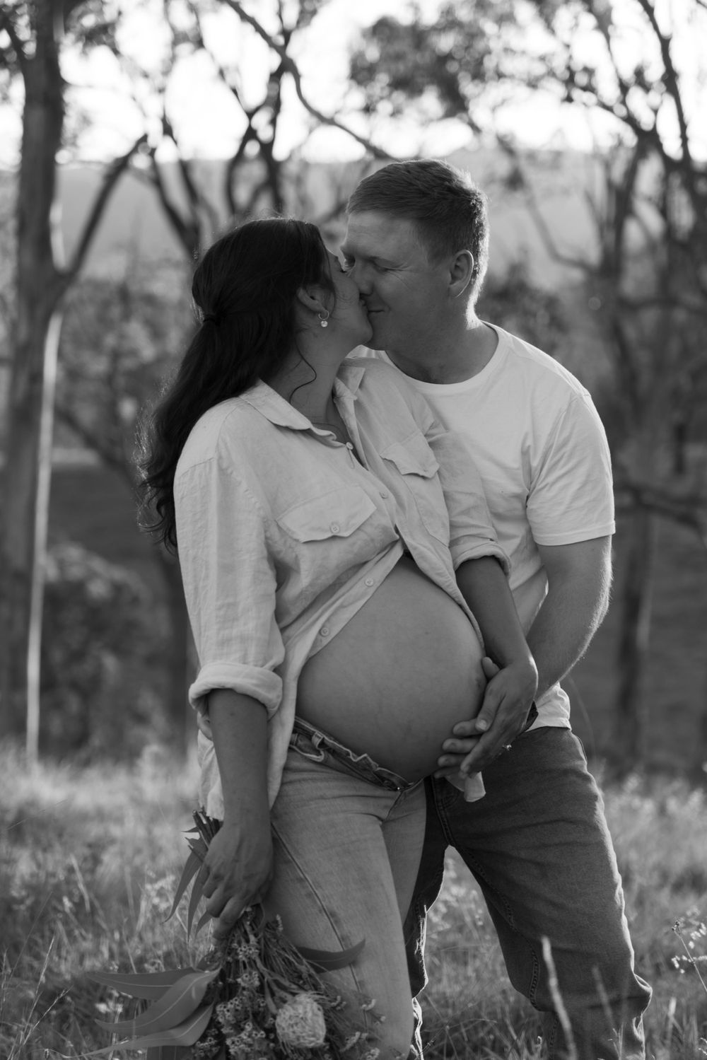 A romantic black and white maternity photo shows an intimate moment between expecting parents outdoors.