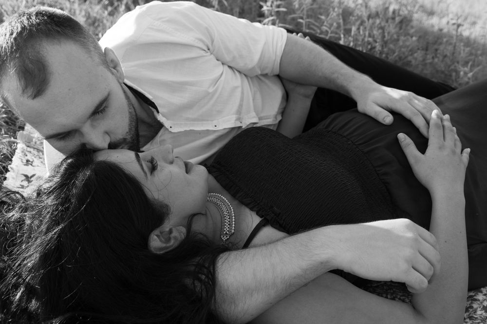Romantic couple sharing tender moments in a field at sunset, while touching pregnant belly.