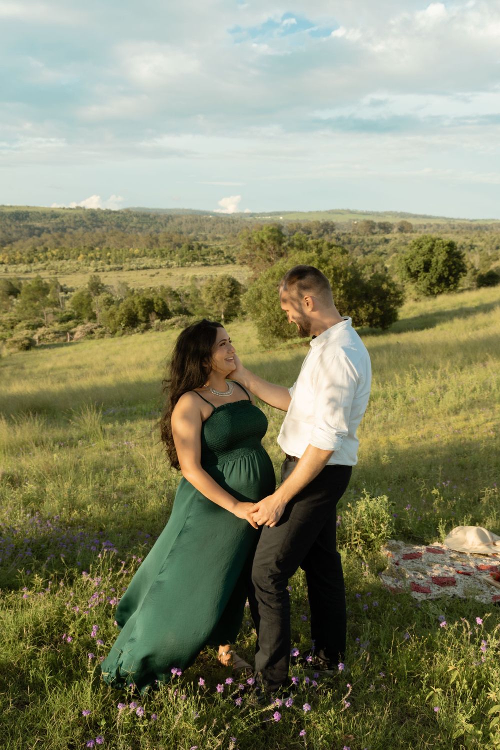 Couple sitting together on grassy hillside during sunset maternity photoshoot.