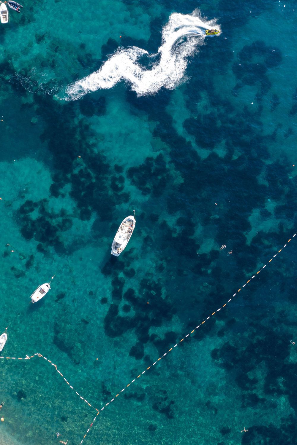 Aerial shot of boats in turquoise waters with white wake patterns creating dragon-like shapes.