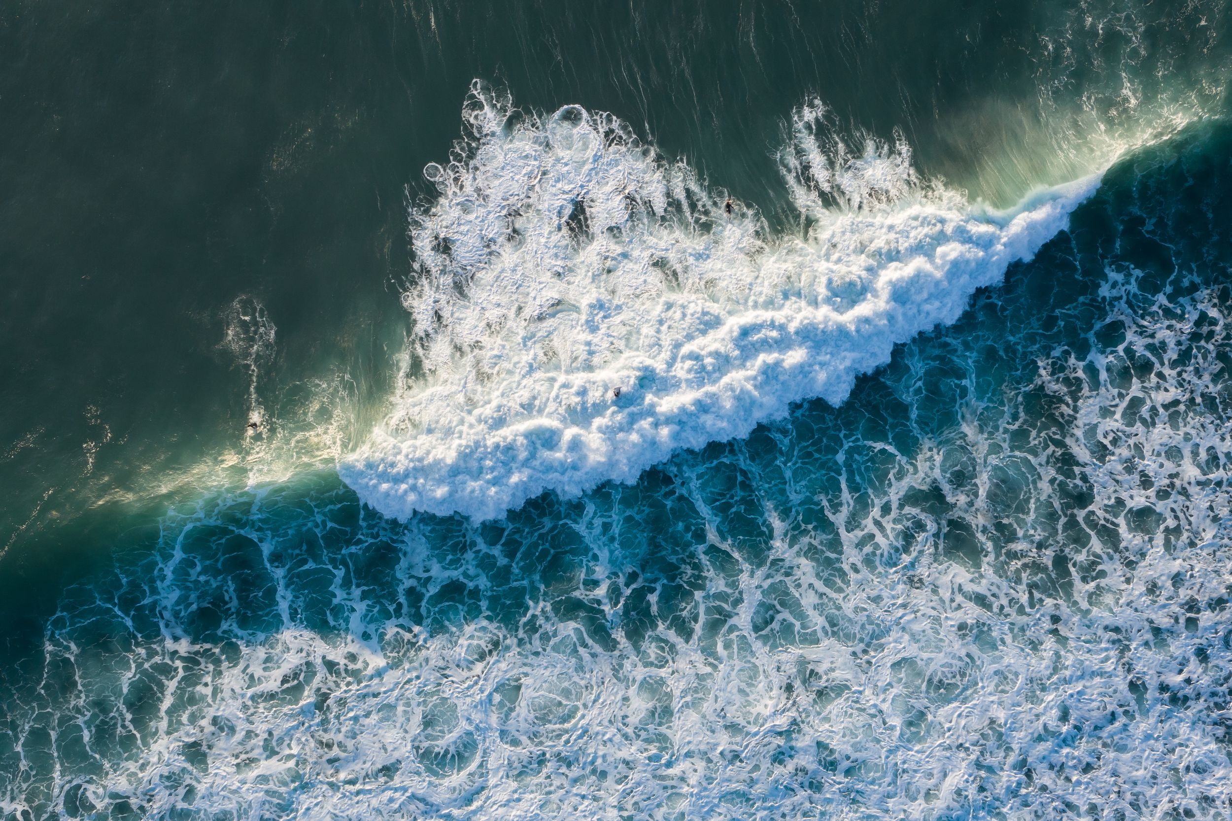 Aerial view of ocean waves crashing with white foam patterns against dark blue water.
