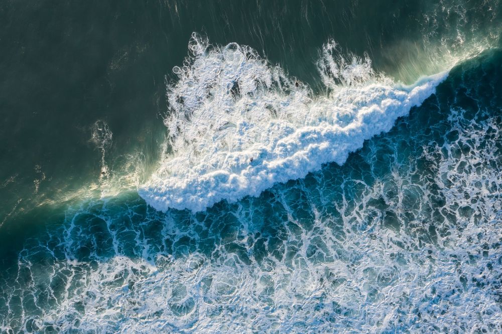 Aerial view of ocean waves crashing with white foam patterns against dark blue water.