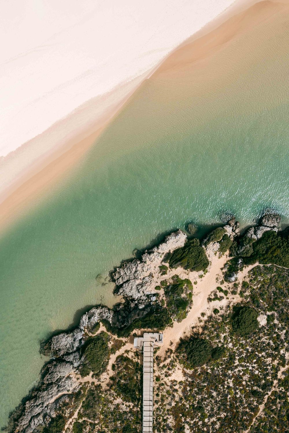 Aerial view of a coastal boardwalk stretching along turquoise waters and sandy beach.