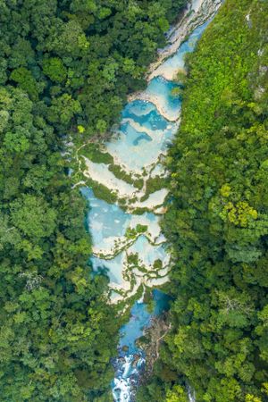 Stunning aerial view of turquoise pools winding through lush green forest in a natural river system.