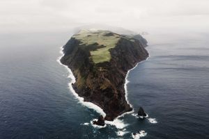 Dramatic aerial view of an isolated triangular island rising from the ocean with steep cliffs.