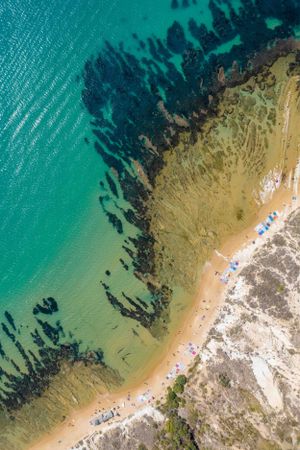 Aerial view of a pristine beach with crystal clear turquoise waters meeting rocky coastal formations.