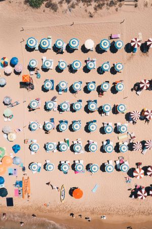 Bird's eye view of neatly arranged blue and white beach umbrellas forming organized rows on golden sand.