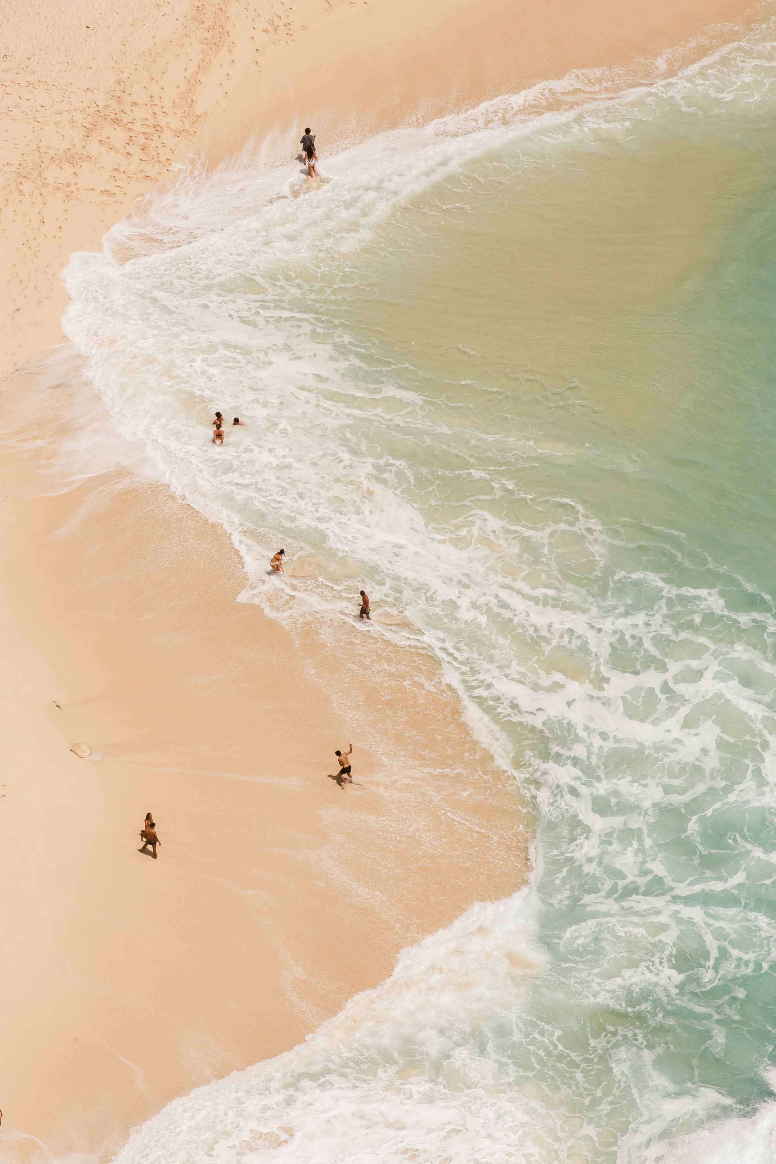 Bird's eye view of people enjoying a beach with turquoise waters and white sand.