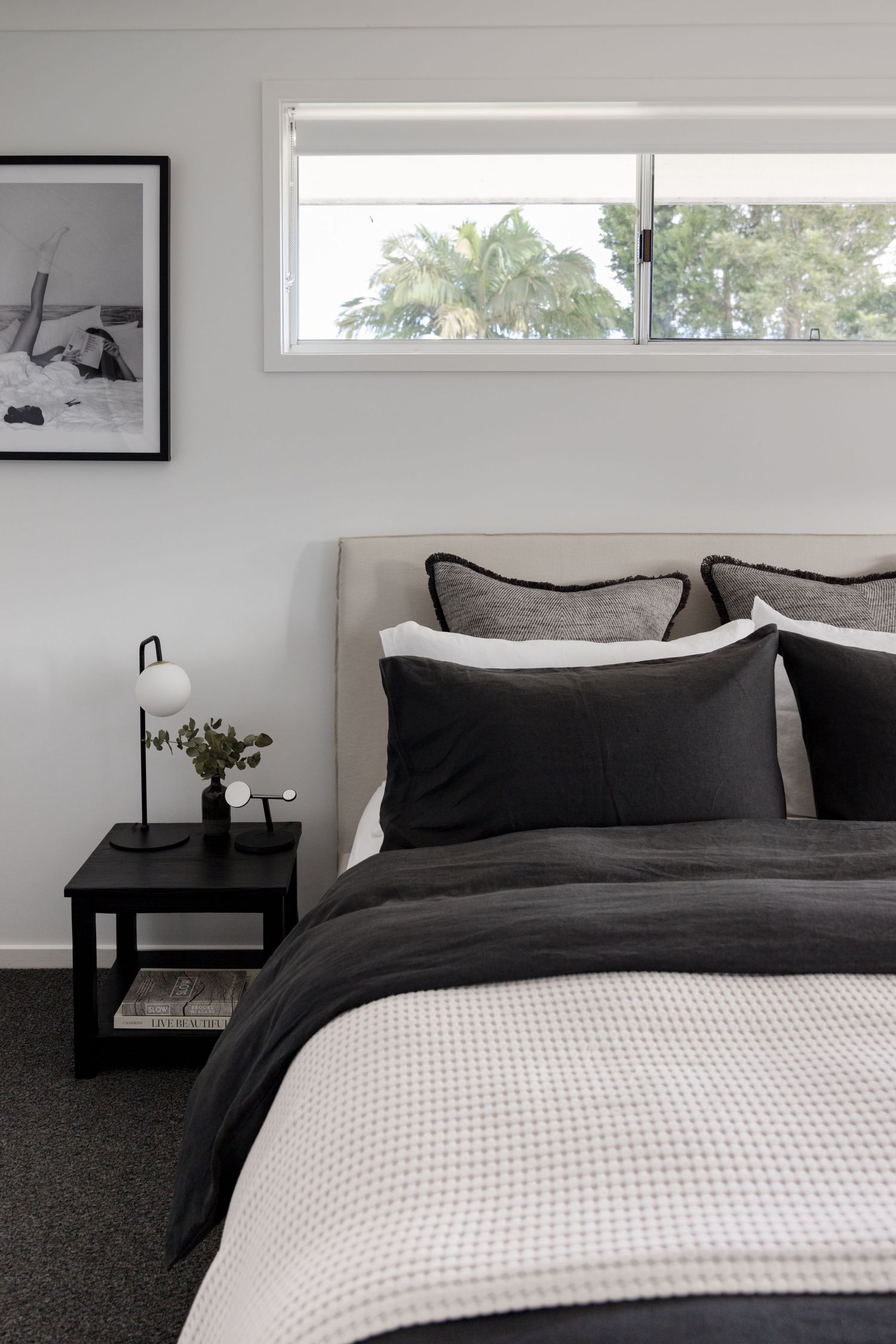 Modern bedroom with monochrome bedding, small black side table and high window.