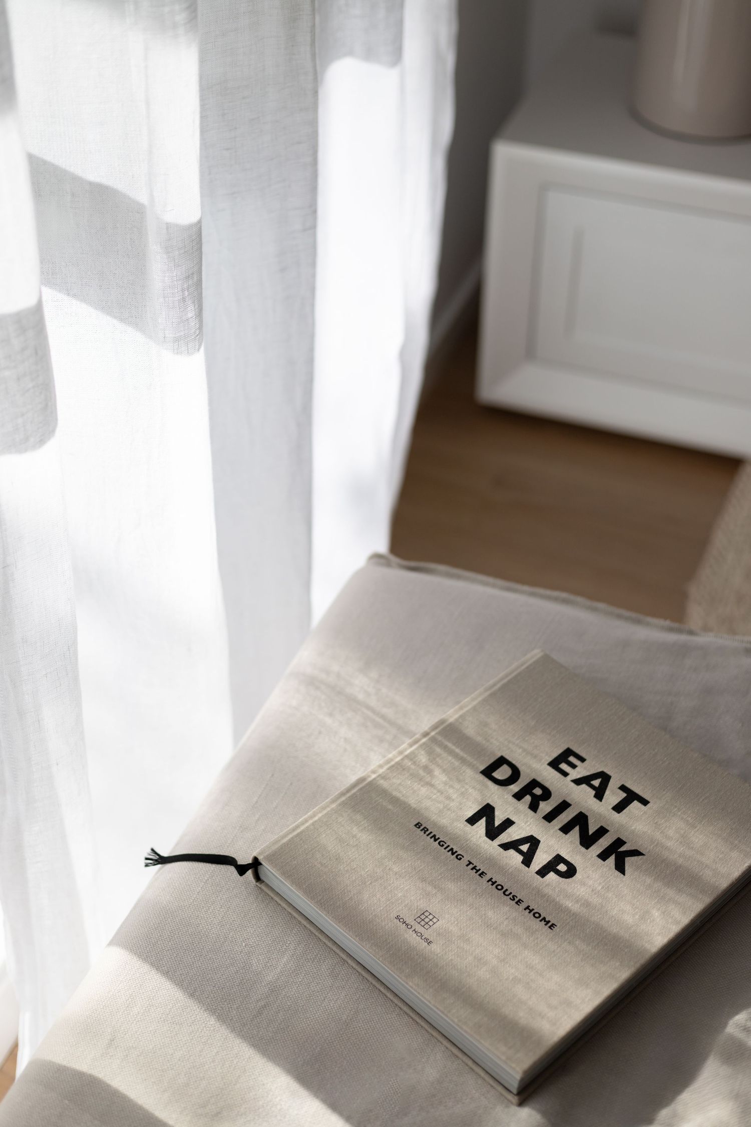 Book titled 'Eat Drink Nap' lying on white fabric near sheer curtains.