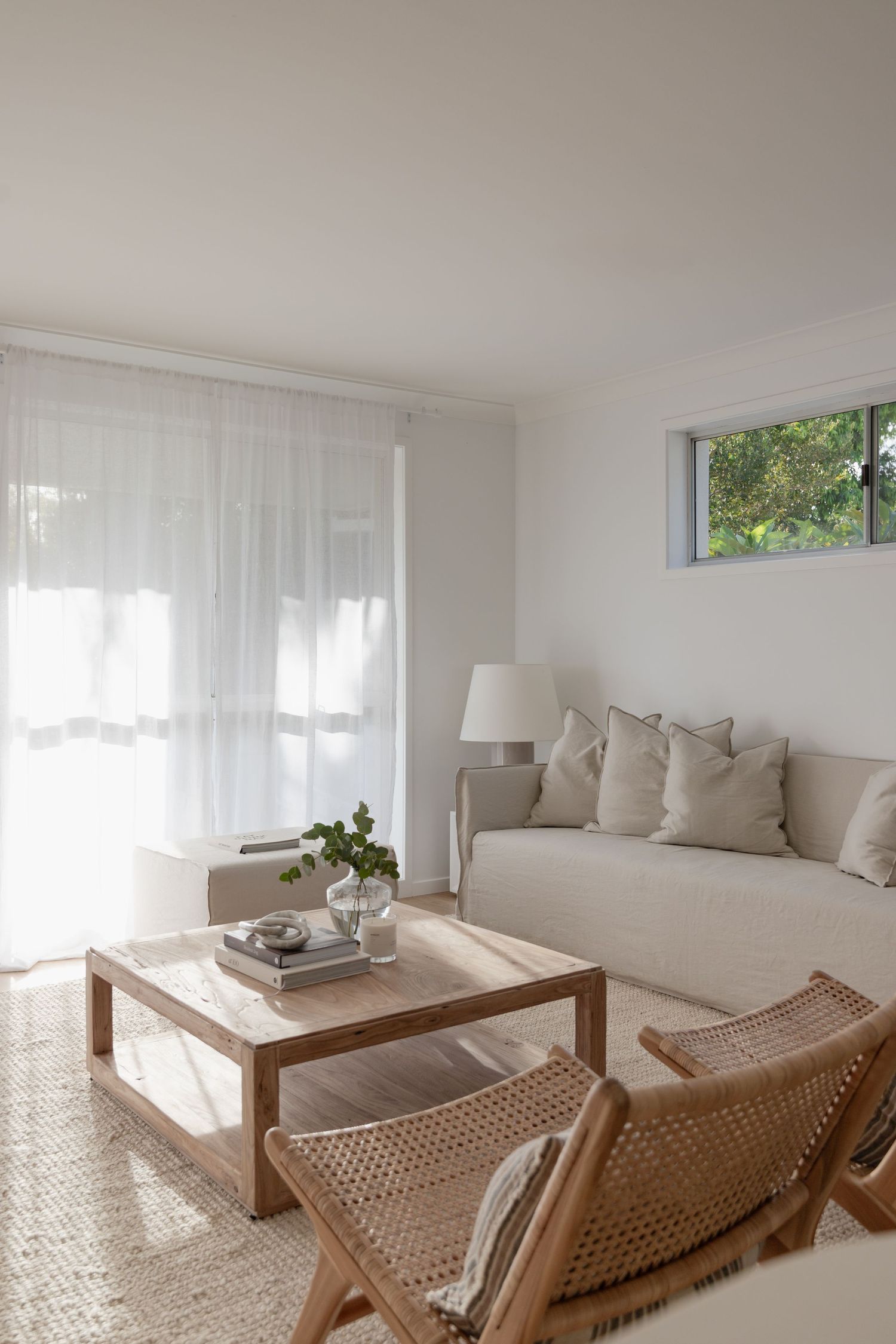Bright living room with sheer curtains, beige sofa, and rattan lounge chair in neutral tones.