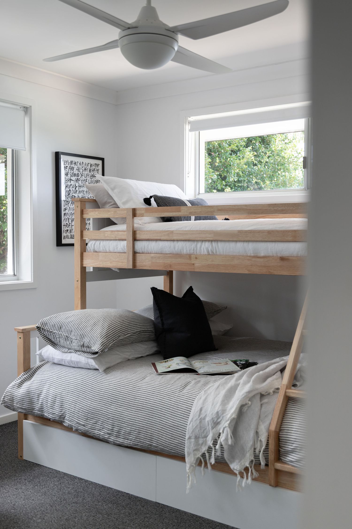 Modern wooden bunk bed with gray bedding and ceiling fan in bright bedroom.
