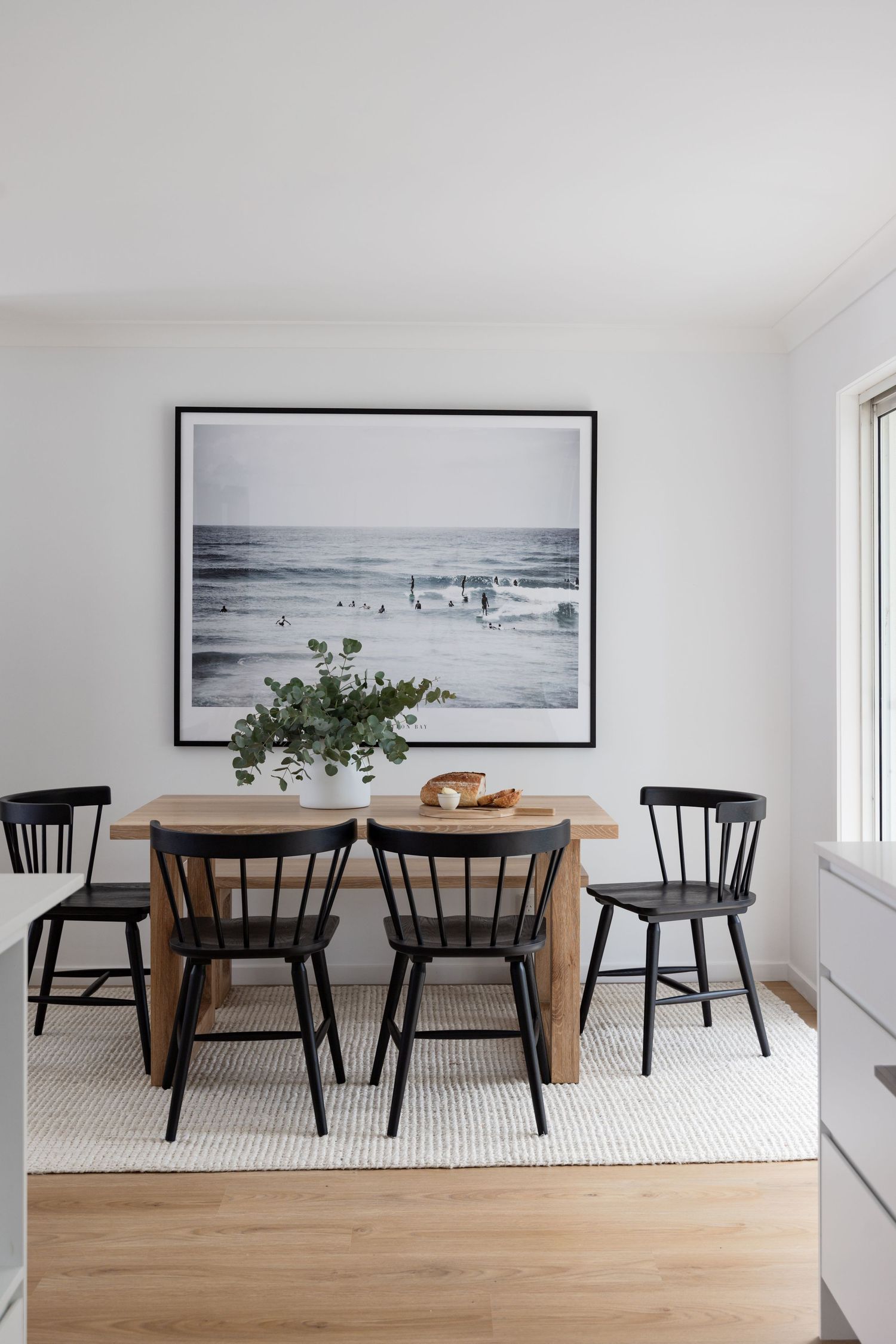 Dining area with black chairs and beach scene artwork on white wall.