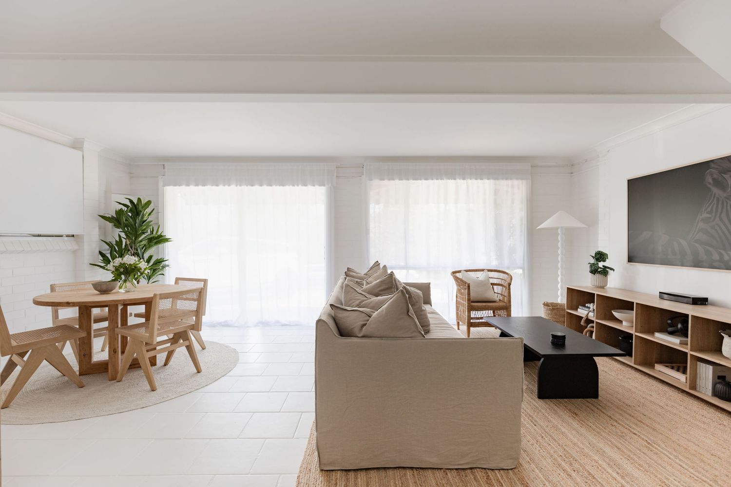 Minimalist living room with beige sofa, wooden dining set, and entertainment center.