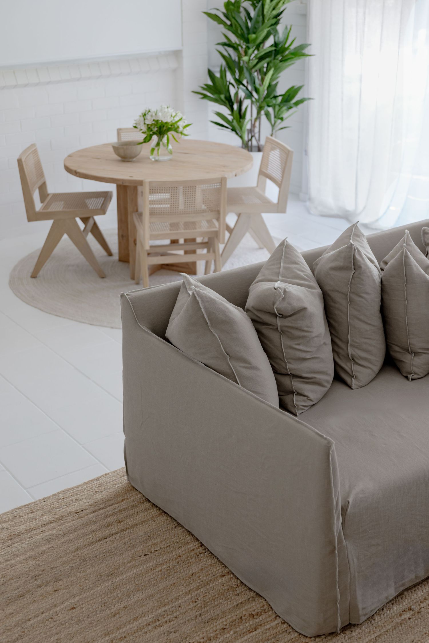 Gray sofa with plush pillows near round wooden dining table and indoor plant.