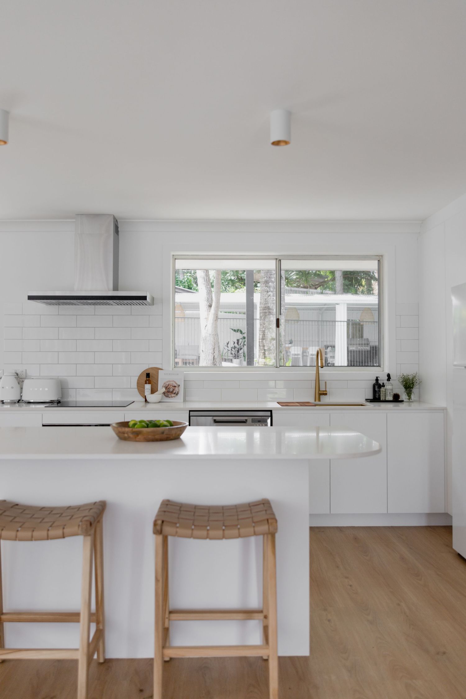 Clean white modern kitchen with wooden bar stools and subway tile backsplash.
