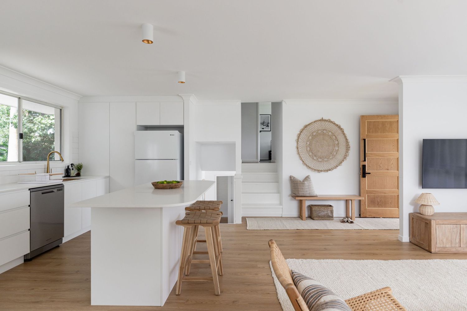 Open concept kitchen and living space with white counters and natural wood accents.