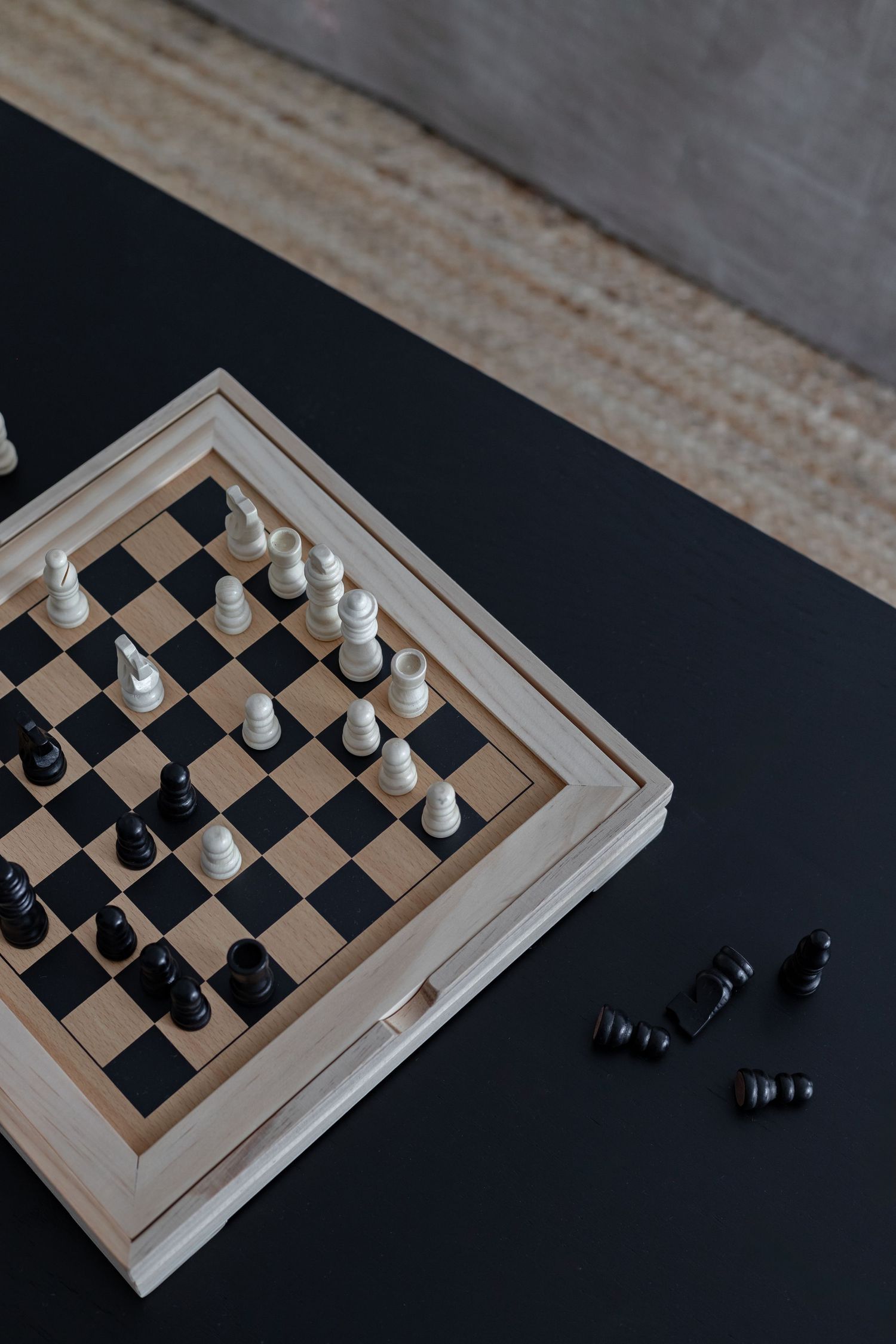 Wooden chess board with white and black pieces on dark surface.