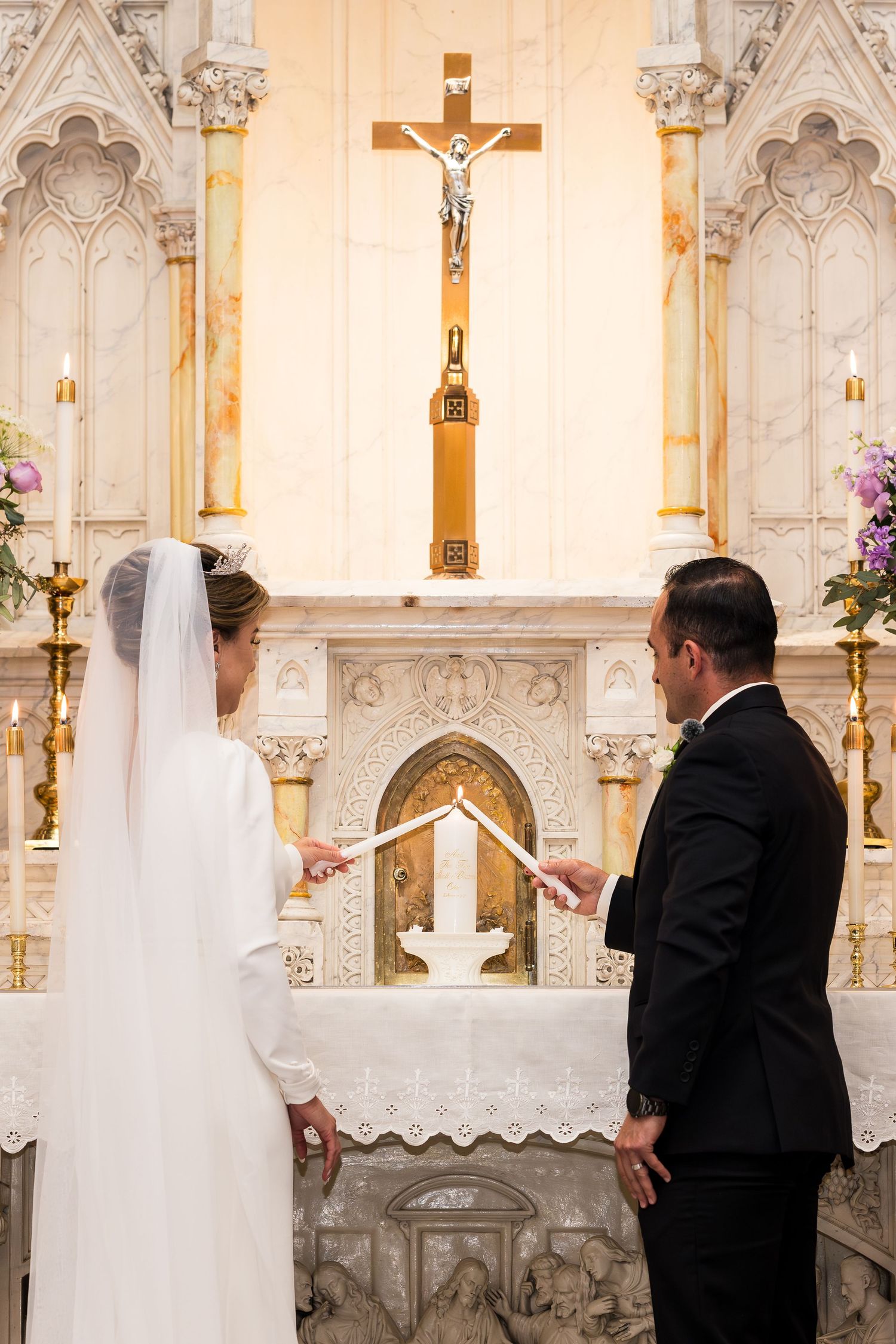 A couple exchanges vows at an ornate church altar with a prominent crucifix.