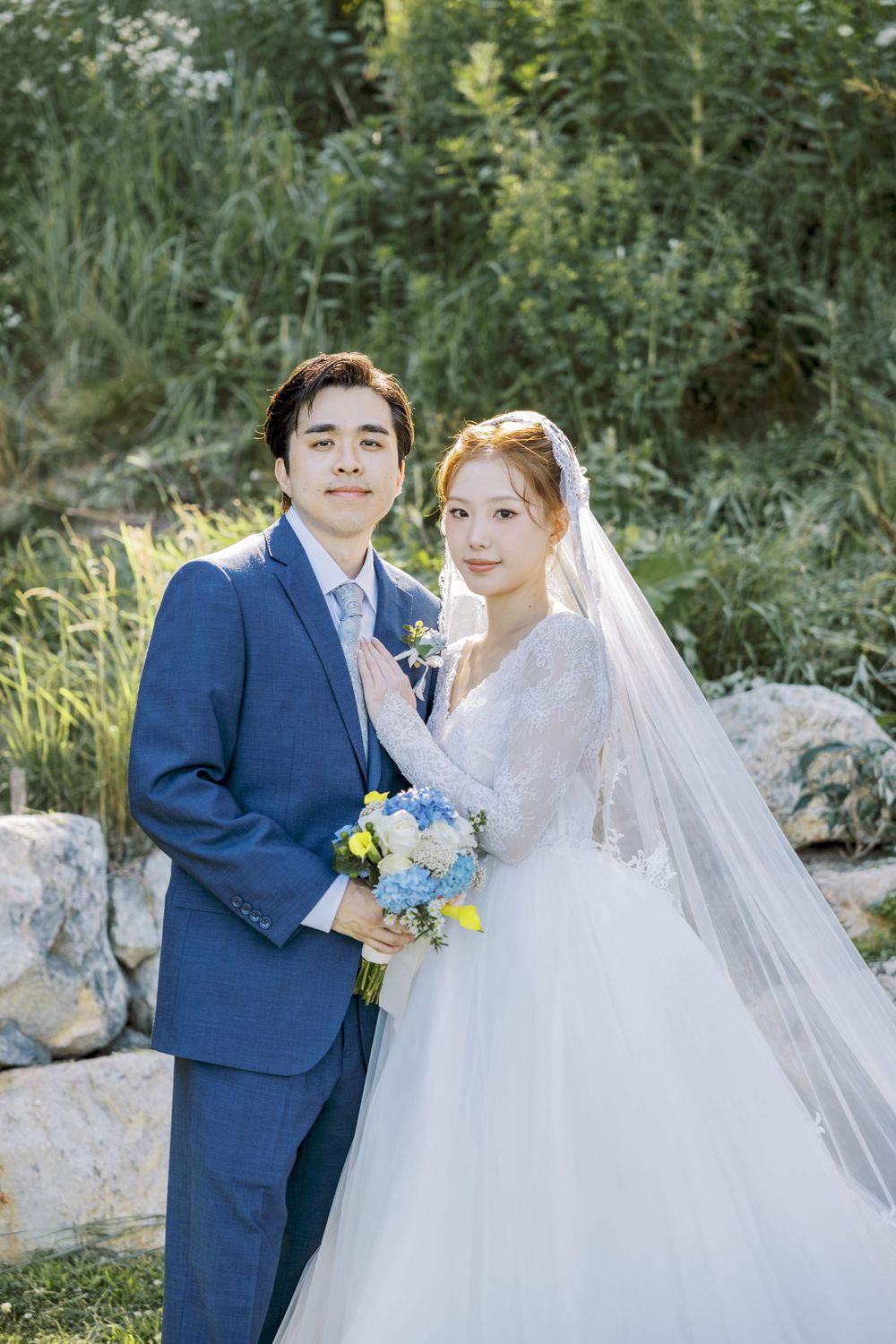 Romantic wedding portrait among green foliage with blue and white color scheme.